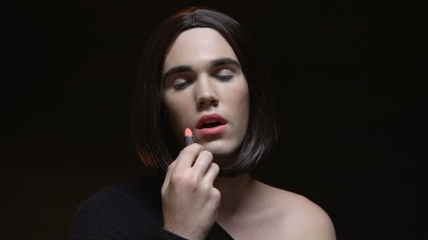 Трансвестит наносить блиск для губ усміхнена камера, перевдягання, чорний фон — стокове відео