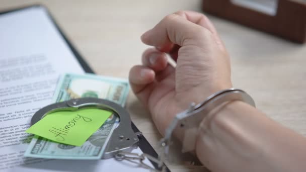 Male hand in cuffs and dollars with alimony sign on table, obligatory payment — Stock Video