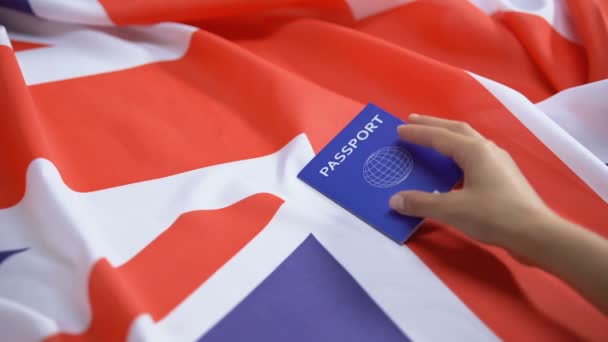 Mano femenina poniendo pasaporte azul internacional en bandera británica, solicitante de visa — Vídeos de Stock