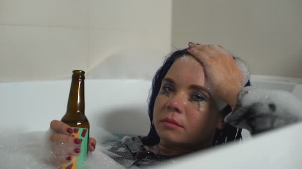 Пьяная женщина с бутылкой пива лежит в ванной, страдает депрессией, жизненные проблемы — стоковое видео