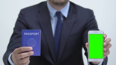 Yeşil ekranlı pasaport ve akıllı telefon tutan yönetici, çevrimiçi kayıt
