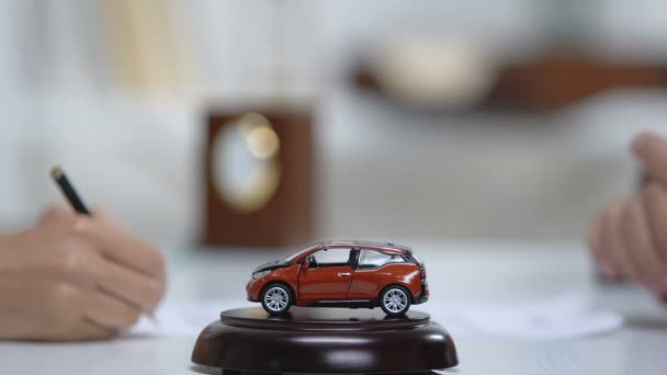 Женщина подписывает документы на продажу автомобилей, автомобильную игрушку на столе, покупку недвижимости — стоковое видео