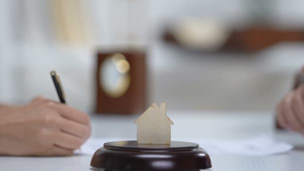 Женщина подписывает документы на квартиру и пожимает руку риэлтору, бумажный дом на столе — стоковое видео