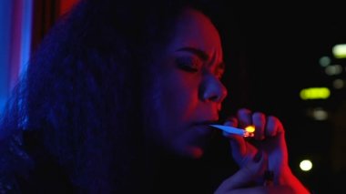 Relaxing young female lighting and smoking weed standing balcony, night life