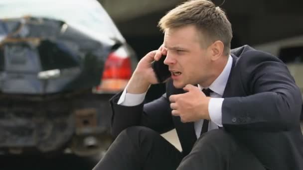 大破した車の背景に電話を話す怒っている男性運転手、自動車事故ストレス — ストック動画