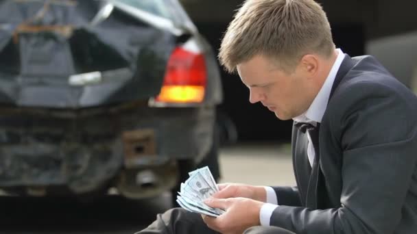 壊れた自動車の背景、自動車事故でドルを数える神経質な男性ドライバー — ストック動画