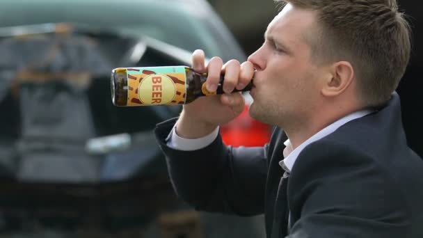 Безответственный мужчина пьет пиво из бутылки на фоне разбившейся машины — стоковое видео