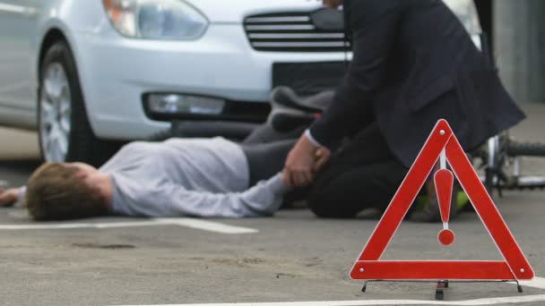 Motorista masculino chamando ambulância, asfalto ciclista inconsciente, sinal de perigo de estrada — Vídeo de Stock