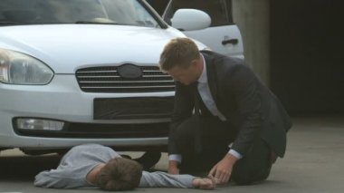 Stressed car driver checking wrist pulse of unconscious pedestrian, road danger