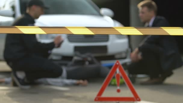 Oficial escribiendo informe de accidente de coche hablando con conductor masculino detrás de cinta de precaución — Vídeos de Stock