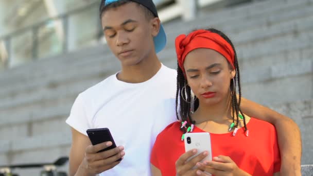 Afro-americano adolescente pareja charlando en los teléfonos inteligentes, falta de comunicación — Vídeo de stock