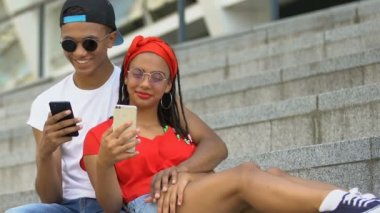 Hugging black teen couple with smartphones laughing from social network jokes
