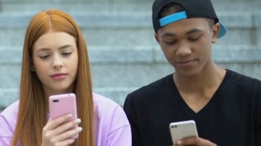 Açık havada akıllı telefonları kaydıran melez erkek ve Kafkas kızıl saçlı kız.