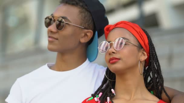 Объятия подростковой пары смешанной расы в солнцезащитных очках, охлаждение на стадионе, время вместе — стоковое видео