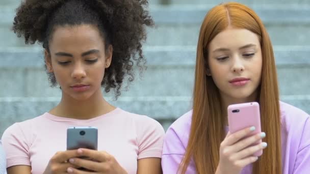 Multietniska kvinnliga tonåringar chattar på smartphones, verklig kommunikationsbrist — Stockvideo