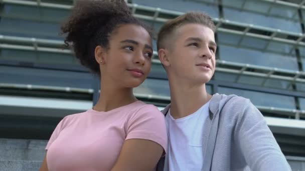 Genç, çok ırklı çift akademi merdivenlerinde kucaklaşıp şehir manzarasından zevk alıyorlar. — Stok video