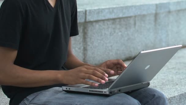 Hombre afroamericano escribiendo en el ordenador portátil PC al aire libre, freelance o estudiando, aplicación — Vídeo de stock