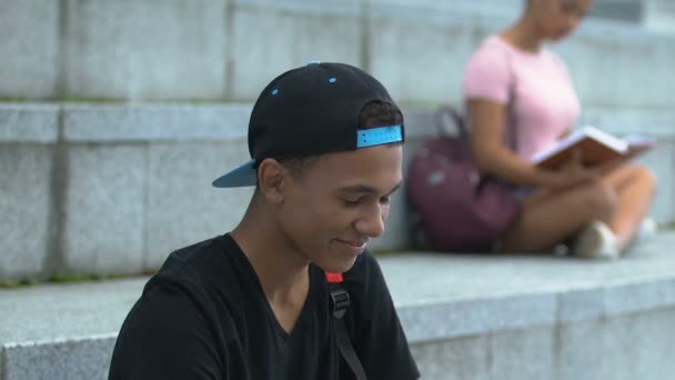 Vrolijke biracial tiener zittende academie trap en glimlachen op camera, onderwijs — Stockvideo