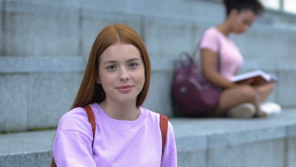 Hermosa estudiante femenina con mochila sonriendo a la cámara, descansando escaleras del campus — Vídeos de Stock