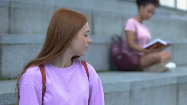 Kampüs merdivenlerinde oturan kararsız beyaz kız öğrenci, zor seçim — Stok video