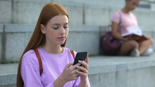 Csinos vörös hajú tinédzser lány sms-ezik mobilon új hírvivő alkalmazás — Stock videók
