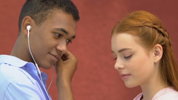 Esmaltado macho adolescente dando auriculares a joven chica, escuchando música juntos — Vídeo de stock
