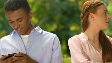 Sinirli genç bir bayan karışık ırktan erkek arkadaşı akıllı telefondan oyun oynuyor.