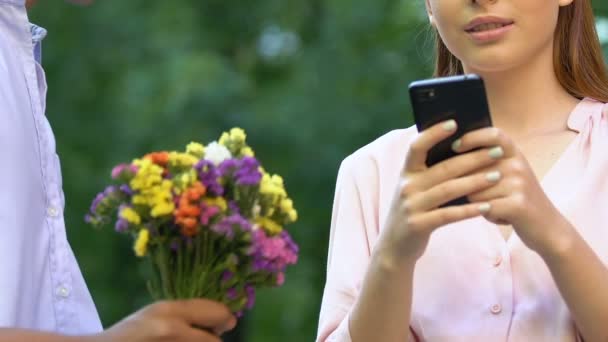 Dziewczyna niedbale biorąc kwiaty od człowieka podczas pisania wiadomości w telefonie, uzależnienie — Wideo stockowe