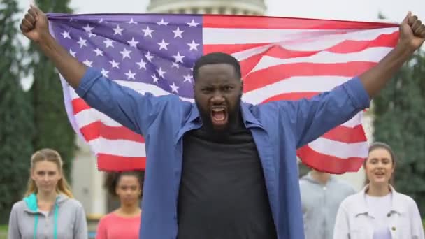 Раздражённый чернокожий, поднимающий американский флаг, антирасистский митинг, миграционный кризис в США — стоковое видео