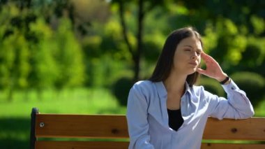 Yorgun kadın bankta dinleniyor, şakaklara masaj yapıyor, baş ağrısı çekiyor, migren ağrısı çekiyor.