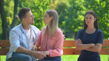 Birbirine aşık çiftler bankta oturup sarılıp sohbet ederler, arkadaşlarını görmezden gelirler.