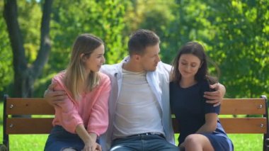 Yakışıklı adam parkta bankta dinleniyor iki çekici kıza sarılıyor, bayan adam.