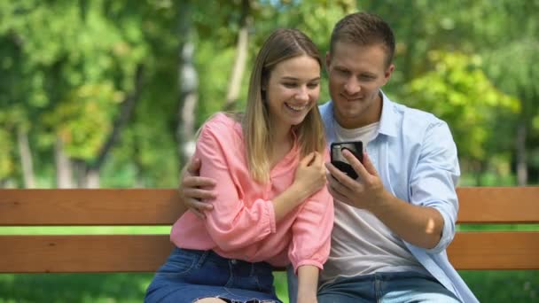 Pareja feliz pasar tiempo juntos en el parque viendo fotos en el teléfono inteligente, fecha — Vídeos de Stock