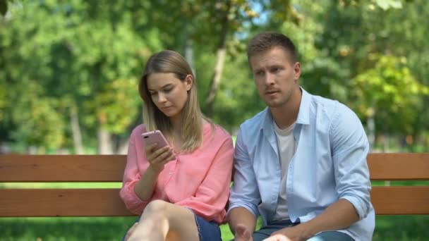 Young woman scrolling phone ignoring man hugging her, problems in relationship — Stock Video