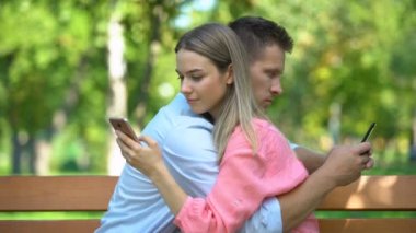 Genç çift parkta sarılıyor, akıllı telefonlarda sohbet ediyor, iletişim eksikliği...