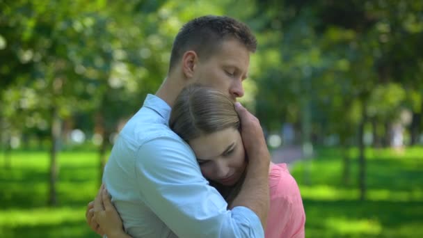 Мужчина обнимает и утешает расстроенную девушку в парке, сплоченность и поддержку — стоковое видео