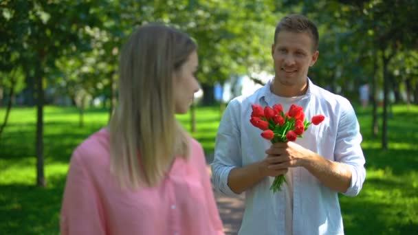 Чоловік приносить дівчині букет квітів, роздратовану леді котиться очима, невизначене кохання — стокове відео