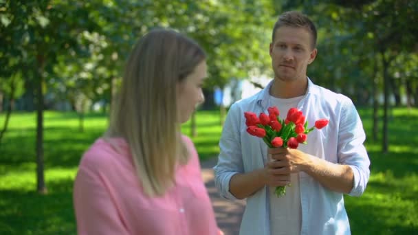 Glad kvinna ler mot kameran, pojkvän med blommor bakom, datum inbjudan — Stockvideo