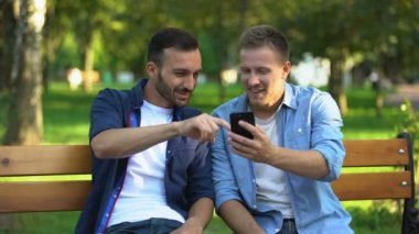 En iyi erkek arkadaşlar akıllı telefondan fotoğraflara bakıyor, parkta eğleniyorlar.