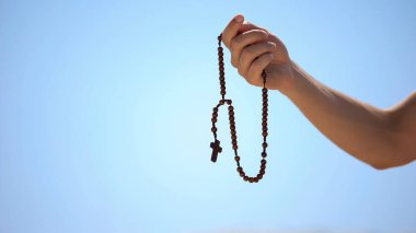 Hand holding rosary, praying to god on blue background, religious spirituality clipart