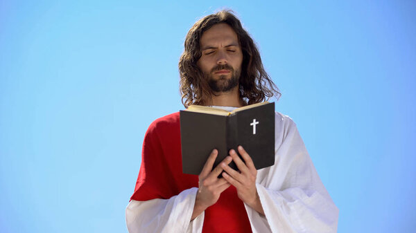 Priest in robe reading Holy Bible, closing eyes to pray, Christian theology