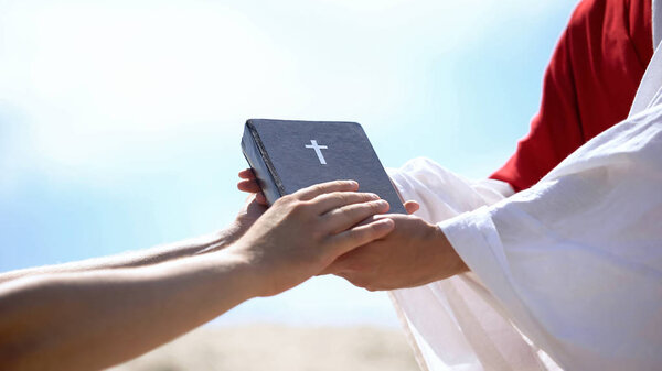 Preacher in robe passing bible to male hands, spreading religious teachings