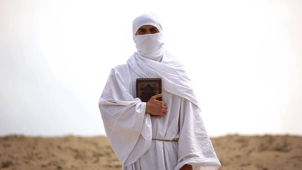 Arab pilgrim holding Koran in desert, preacher of Islamic faith and teachings