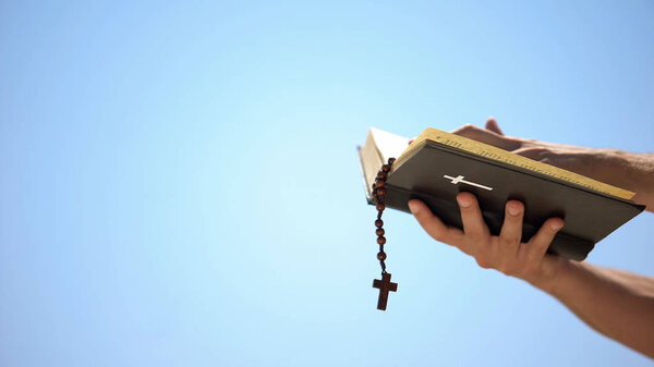 Hands holding bible and rosary on blue background, praying to god, template