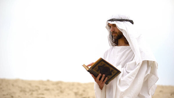 Arab reading Koran in desert, meditating and reflecting on Muhammad teachings