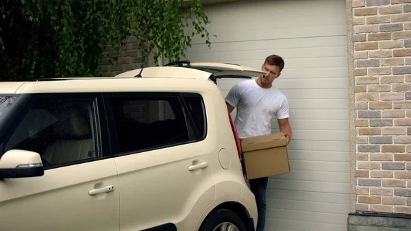 カジュアルな男性が車の中に段ボール箱を入れて 新しい家 不動産に引っ越す — ストック写真