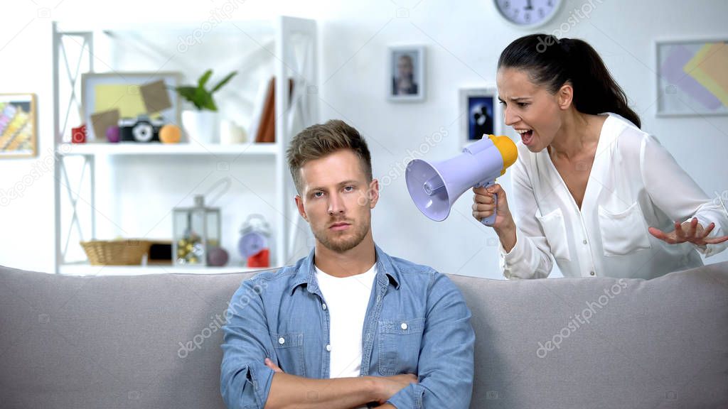 Woman with megaphone shouting on man at home, unsuccessful marriage, conflict