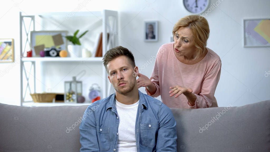 Mother scolding adult son sitting at home on sofa, unfulfilled moms dreams
