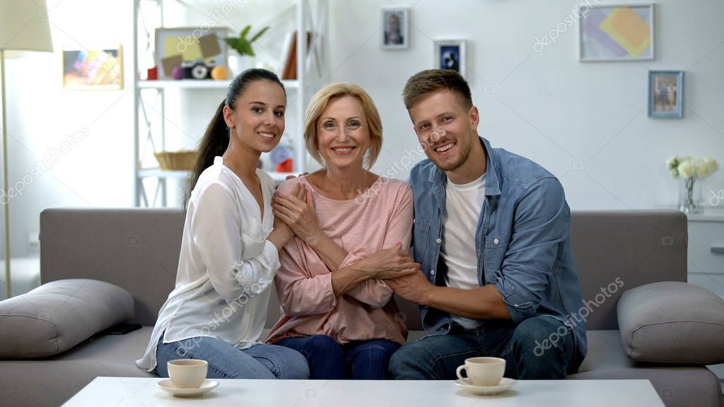 Young couple and mother in law holding hands, smiling at camera, happy together
