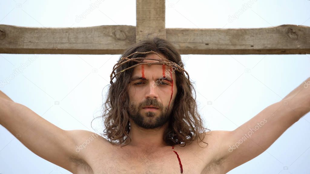 Jesus crucified on wooden cross, bloody head with crown of thorns, sacrifice
